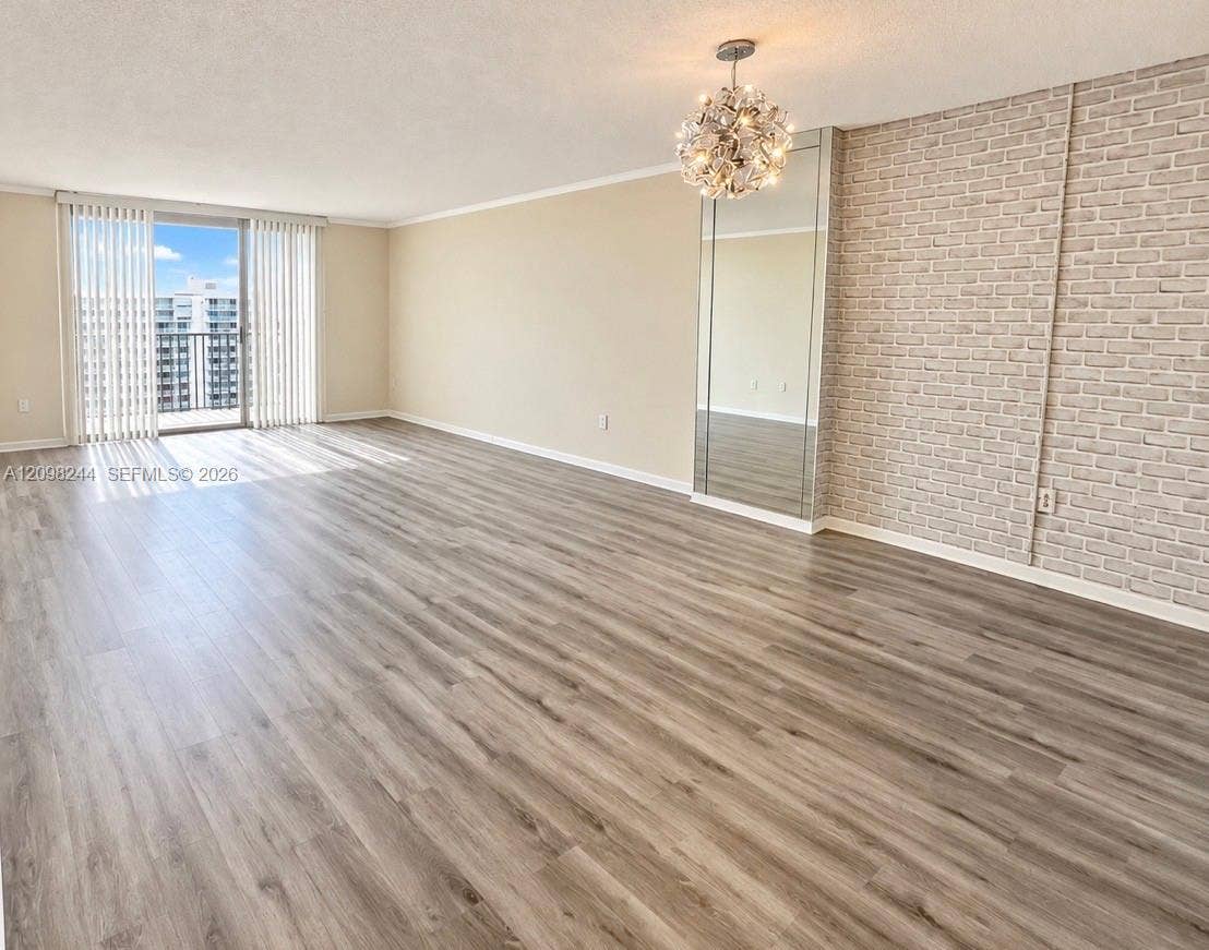 2851 NE 183rd Street, #2110E, Aventura, Aventura, FL 33160 Living area featuring wood-finish flooring, a textured brick accent wall, a floor-to-ceiling mirror panel, a decorative chandelier, and sliding glass balcony doors