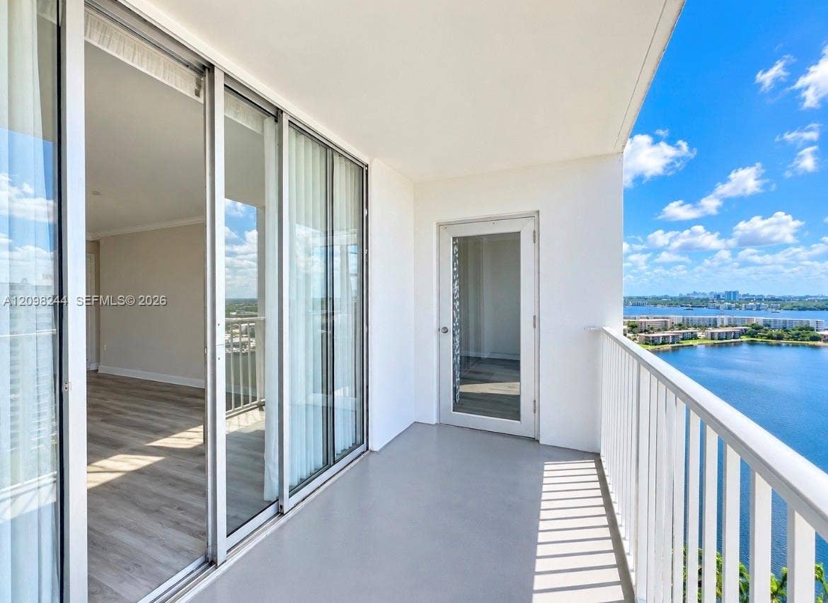 2851 NE 183rd Street, #2110E, Aventura, Aventura, FL 33160 Covered balcony featuring a white metal railing, solid surface flooring, and a glass-paned door, complemented by large sliding glass doors and expansive water scenery