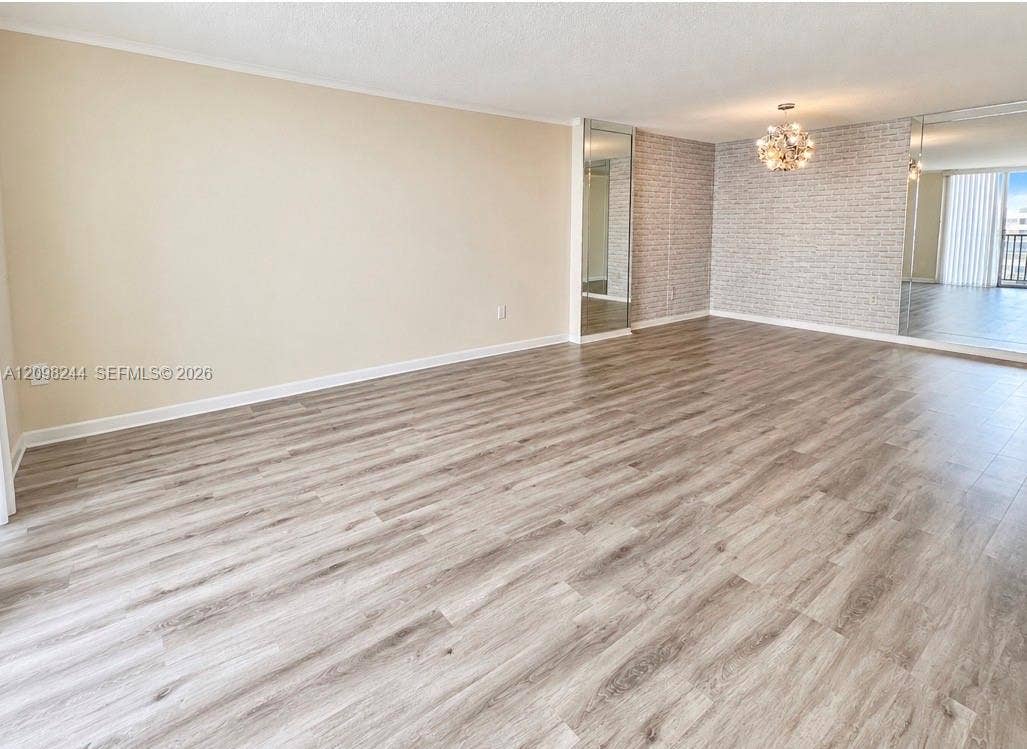 2851 NE 183rd Street, #2110E, Aventura, Aventura, FL 33160 Open-concept interior featuring wood-finish flooring, a decorative textured feature wall, wall-to-wall mirrored panels, and a multi-bulb flush-mount chandelier