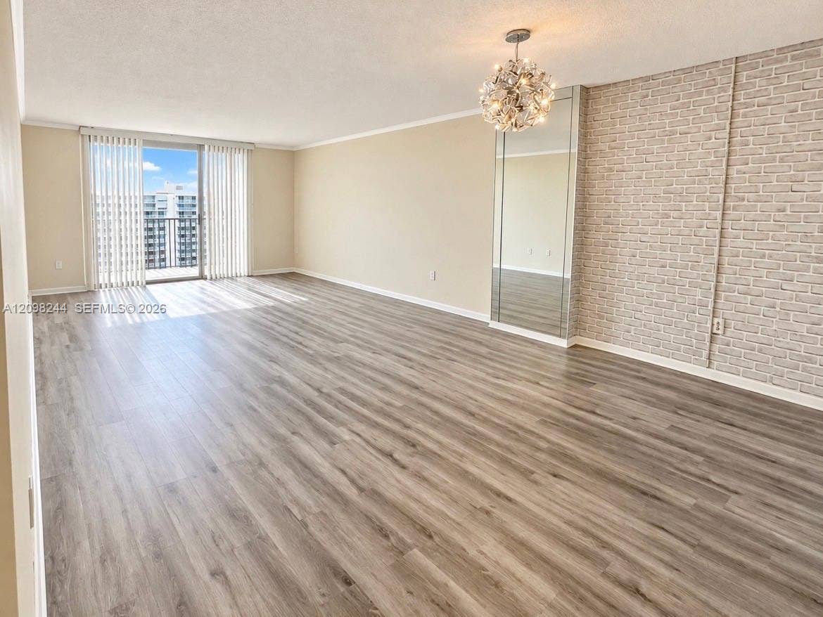 2851 NE 183rd Street, #2110E, Aventura, Aventura, FL 33160 Open-concept living space featuring wood-finish flooring, a textured brick accent wall, mirrored wall paneling, a modern chandelier, and sliding glass doors