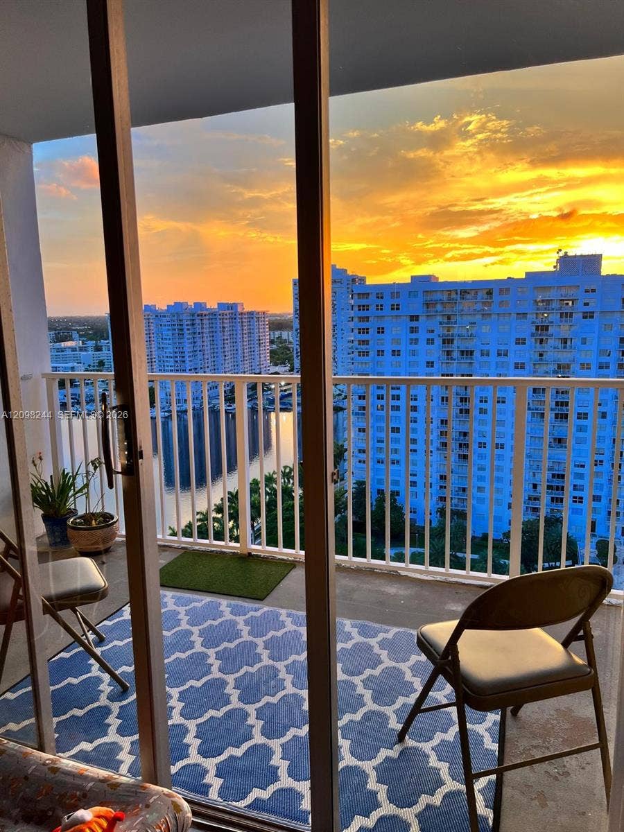 2851 NE 183rd Street, #2110E, Aventura, Aventura, FL 33160 Private balcony featuring metal railings and concrete flooring with a backdrop of urban high-rises, waterfront scenery, and sunset skies