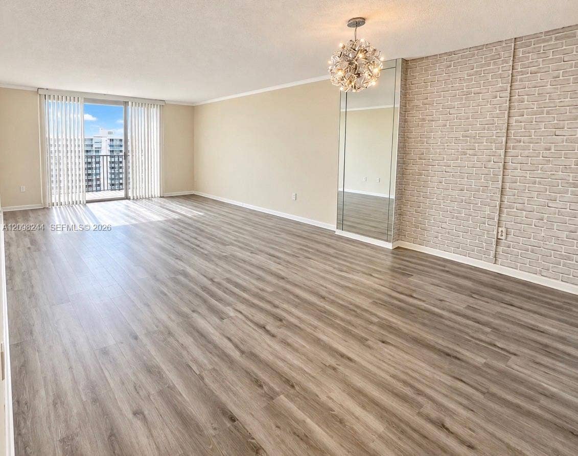 2851 NE 183rd Street, #2110E, Aventura, Aventura, FL 33160 Expansive interior space featuring wood-finish flooring, a textured brick-patterned accent wall, a floor-to-ceiling mirrored panel, a tiered multi-light chandelier, and floor-to-ceiling sliding glass doors