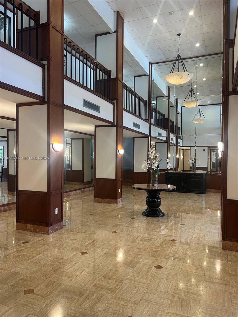 2851 NE 183rd Street, #2110E, Aventura, Aventura, FL 33160 Double-height foyer featuring polished stone flooring with decorative inlays, expansive wall mirrors, dark wood-finished paneling, black metal railings, and three tiered pendant light fixtures
