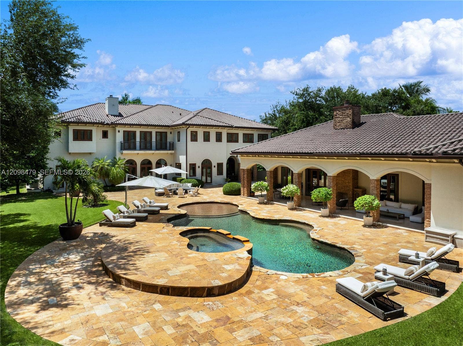 Expansive backyard featuring a custom free-form pool, integrated spa, sprawling stone-paved patio, and a covered loggia with stone-finished pillars