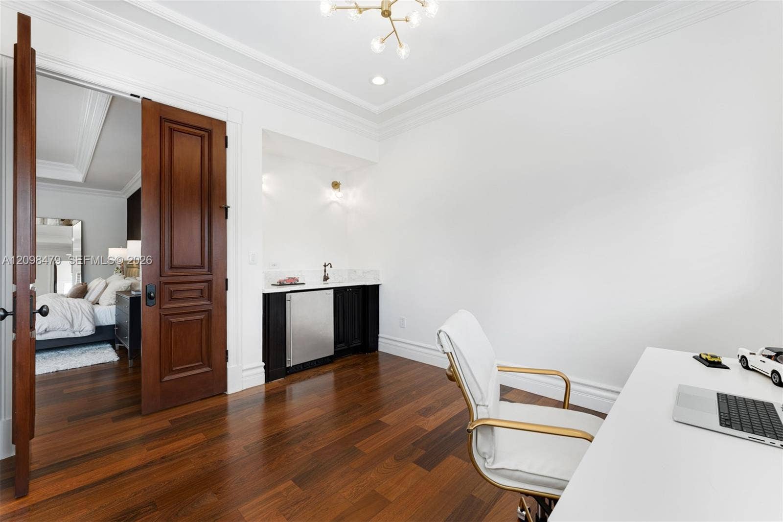 Hardwood flooring, crown molding, built-in wet bar with beverage refrigerator, solid wood paneled doors, and a decorative ceiling light fixture