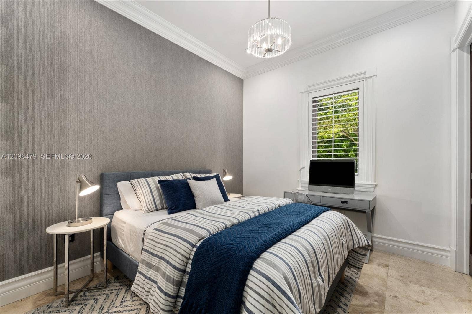 Textured accent wall, crown molding, crystal chandelier, plantation shutters, and light-toned tile flooring