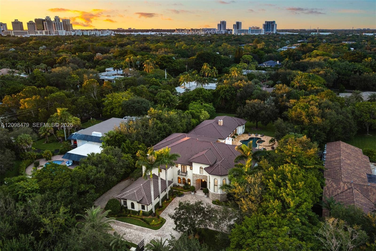 Aerial view of a multi-level estate featuring a tile roof, light-toned masonry exterior, paver driveway, and a backyard swimming pool