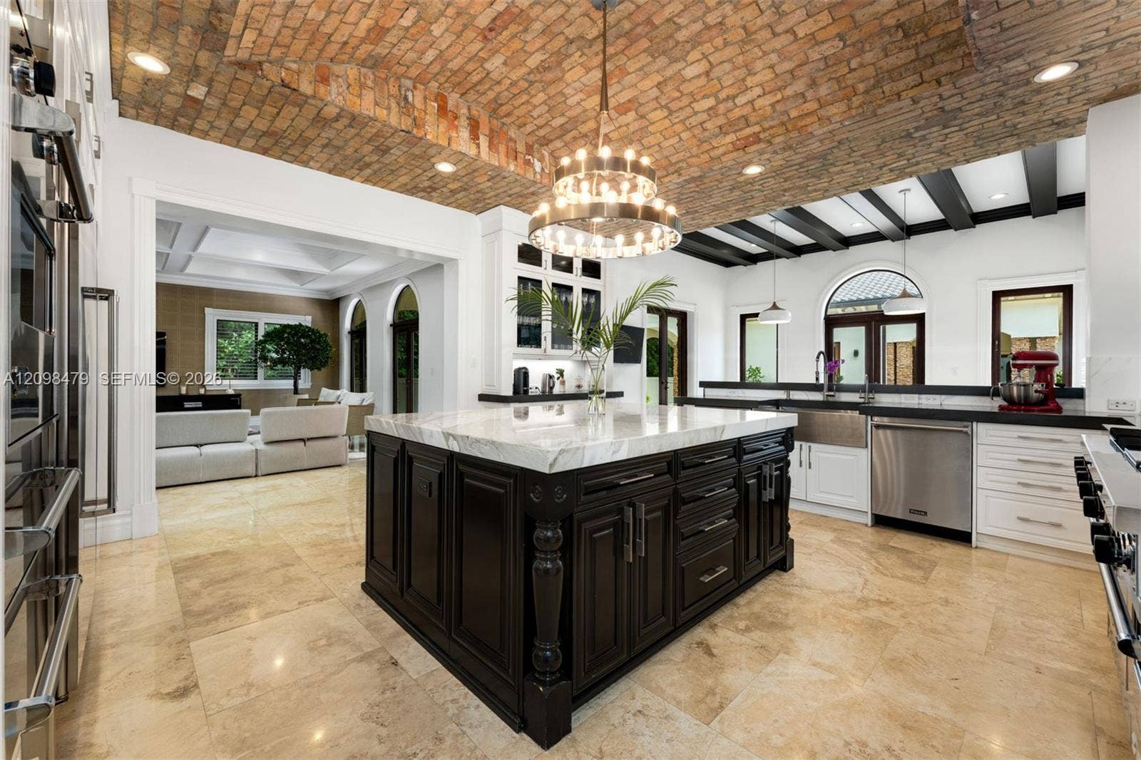Vaulted brick ceiling, large central island with light-toned countertop, stainless steel appliances, dark wood island cabinetry, and light-toned floor tiles
