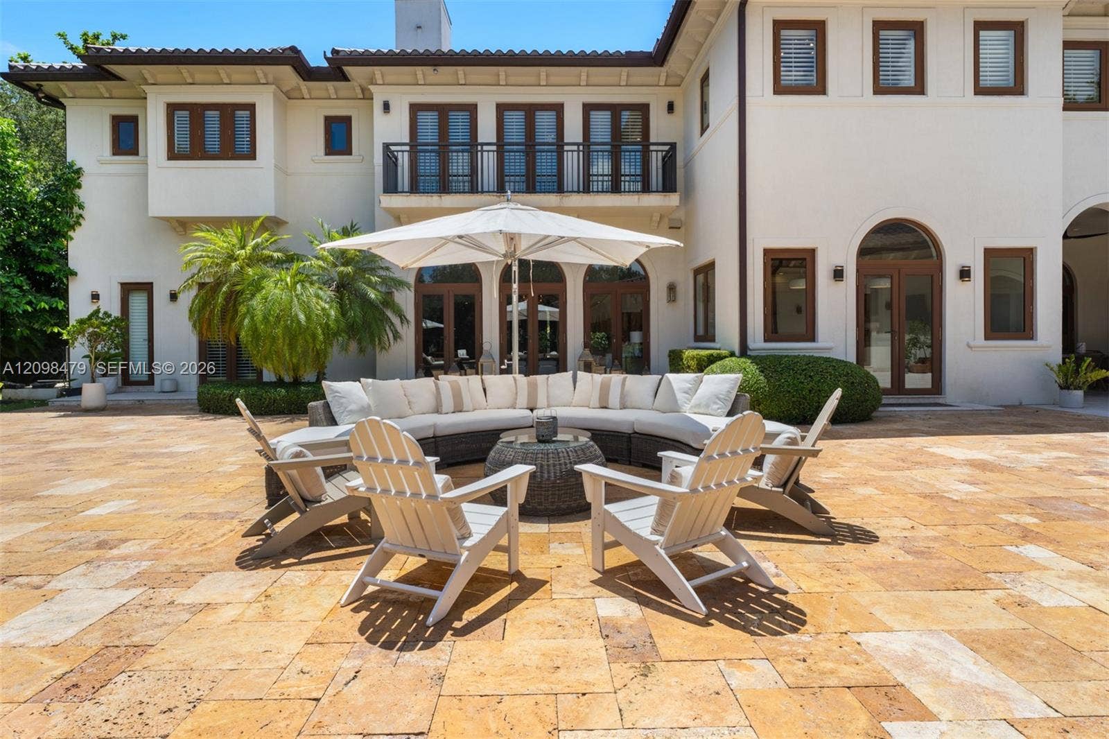 Expansive outdoor patio with large format stone pavers, stucco exterior, and multiple arched and rectangular glass-paned doors