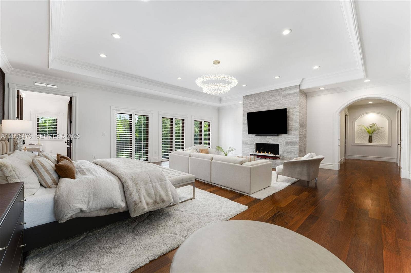 Hardwood flooring throughout, tray ceiling with recessed lighting, stone-clad fireplace, multiple sliding glass doors, and an arched entry