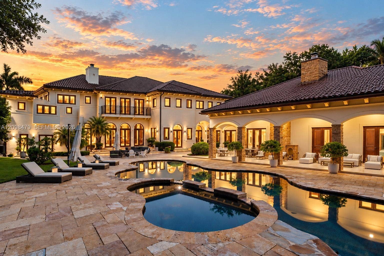 Mediterranean-inspired estate featuring a sprawling stone-paver pool deck, a freeform swimming pool, a covered lanai with arched architectural detailing, and a multi-story stucco exterior with a tile roof