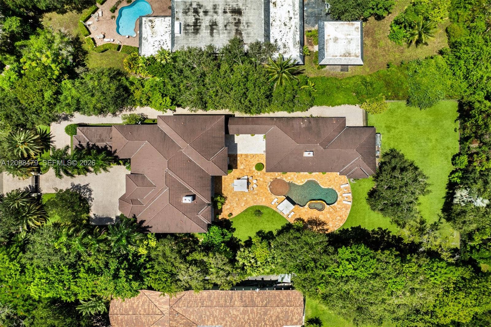 Expansive property featuring a multi-gabled roofline, a large freeform swimming pool with a surrounding paved deck, and a spacious lawn area