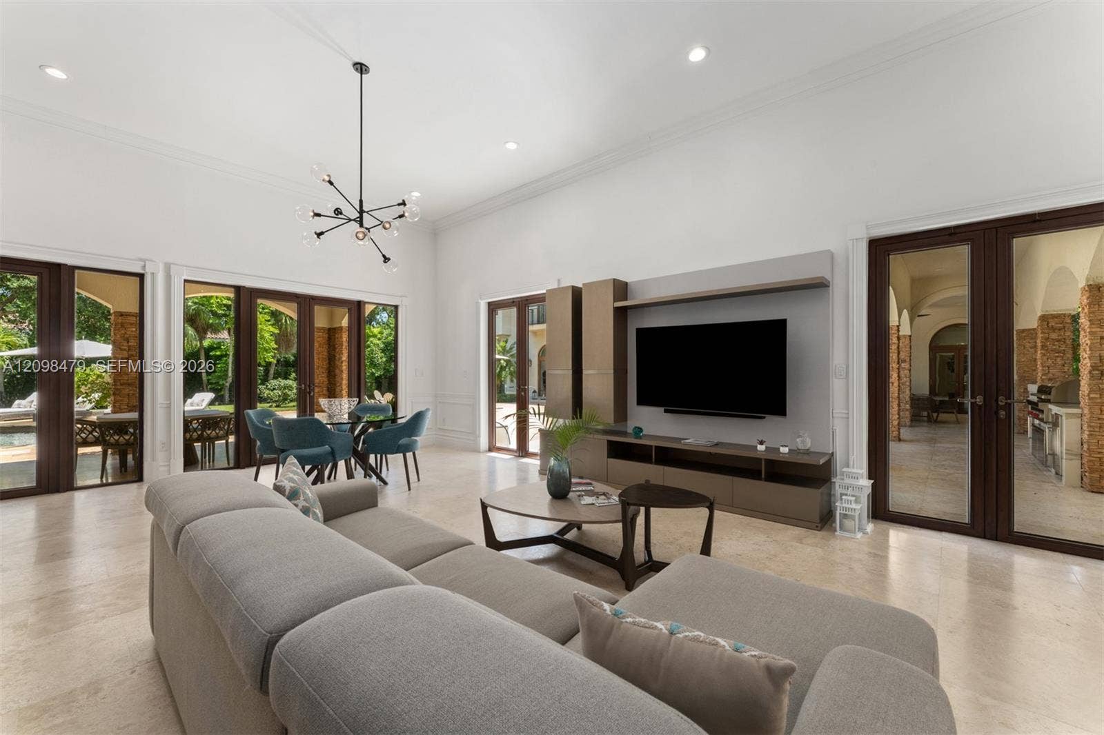 High ceilings with crown molding, stone-finish flooring, multiple sets of glass French doors, and an open-concept living and dining area
