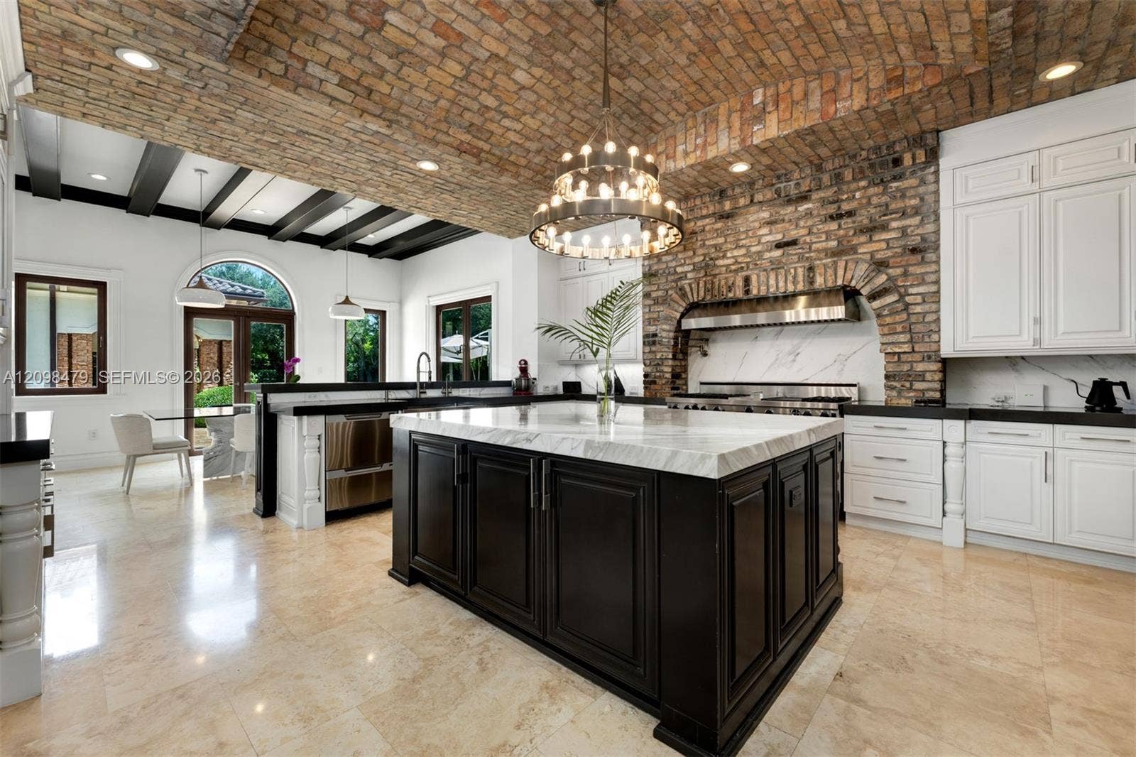 Exposed brick vaulted ceiling with recessed lighting, large central kitchen island with light-colored countertop, white cabinetry, dark stone countertops, and arched brick range hood