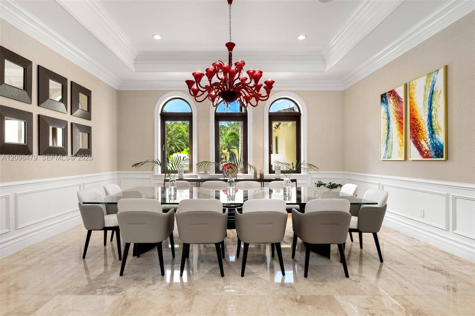 Recessed ceiling with layered crown molding, arched windows, wainscoting, and large format tile flooring