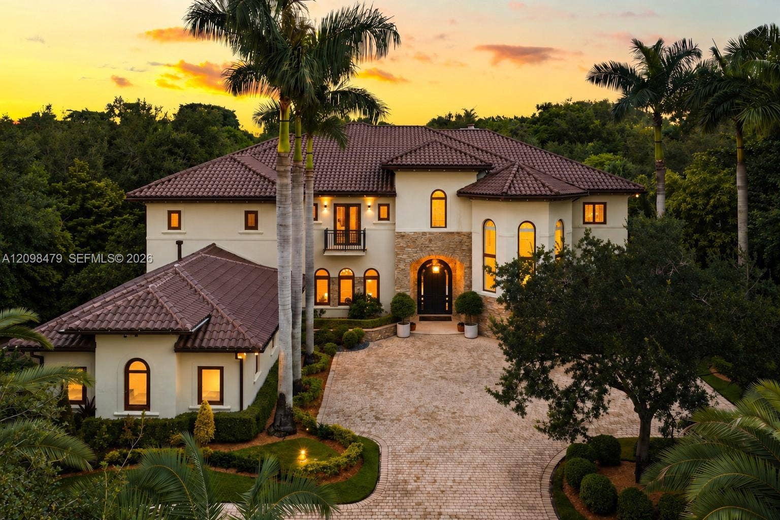 Stucco exterior featuring a tile roof, stone masonry accents, arched window detailing, and a paved motor court