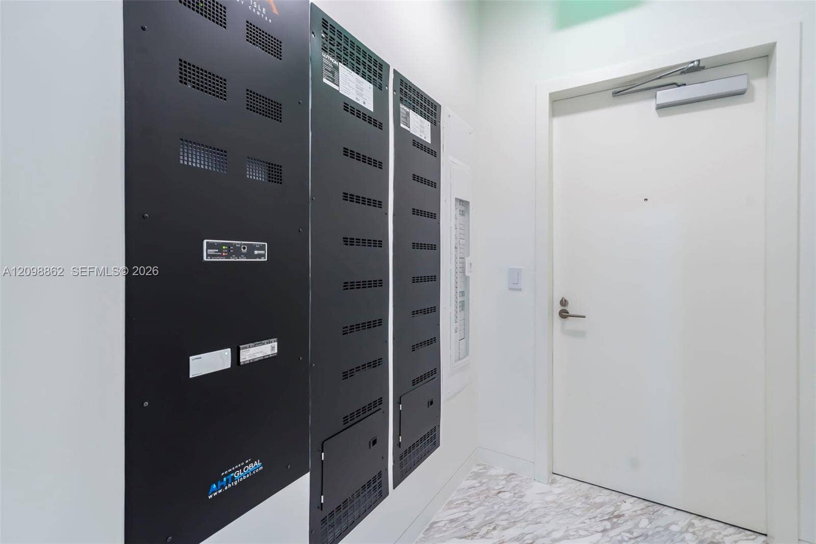 Utility closet featuring integrated technology panels, recessed electrical distribution equipment, and a solid-core door with a hydraulic closure mechanism