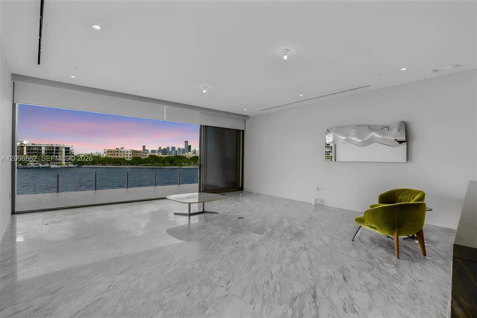Polished stone flooring, expansive floor-to-ceiling glass sliding doors, recessed ceiling lighting, and a private balcony overlooking the water and urban skyline