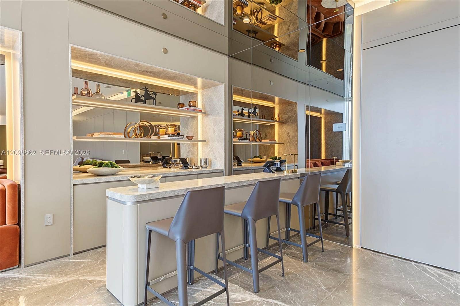 Built-in bar featuring stone-finish countertops, illuminated recessed shelving, full-height mirrored wall panels, and polished stone flooring