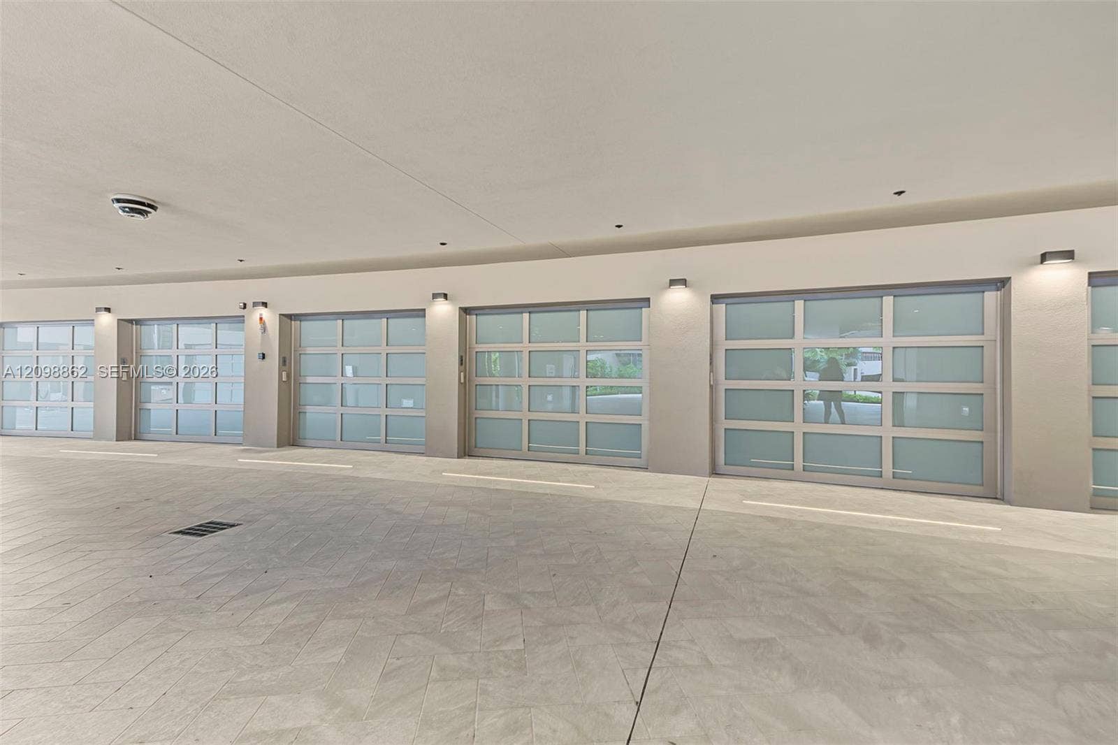 Multi-bay garage featuring frosted glass sectional doors, herringbone-patterned stone flooring, and wall-mounted exterior sconces