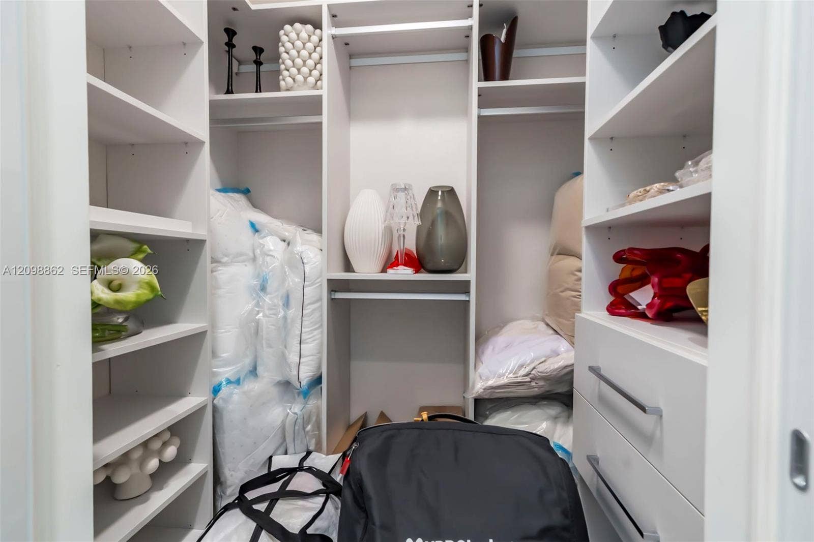 Custom walk-in closet featuring white built-in shelving, integrated hanging rods, and two soft-close storage drawers with metallic pulls