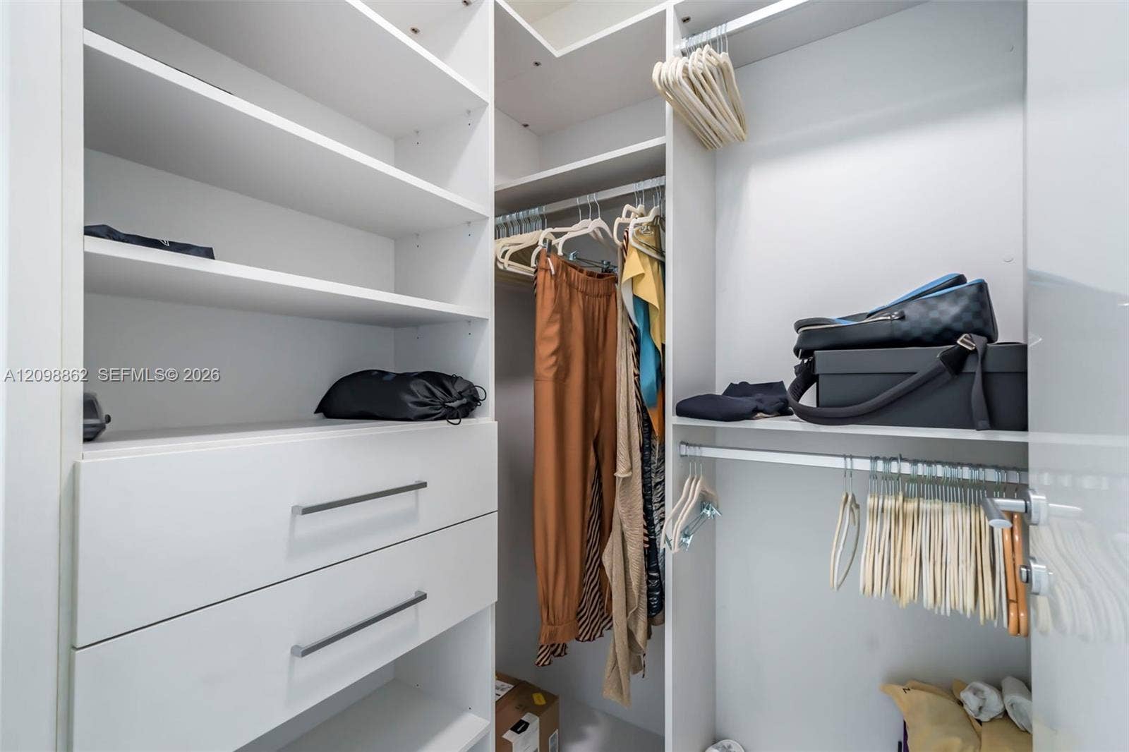 Walk-in closet featuring white built-in cabinetry, dual pull-out drawers with minimalist hardware, adjustable shelving, and multi-level hanging rods
