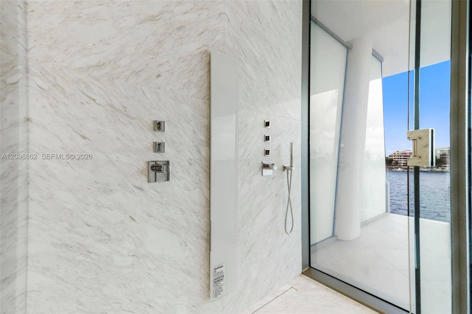 Walk-in shower featuring large-format stone wall tiling, polished chrome wall-mounted fixtures, a minimalist integrated vertical shower panel, and floor-to-ceiling glass paneling with direct water access