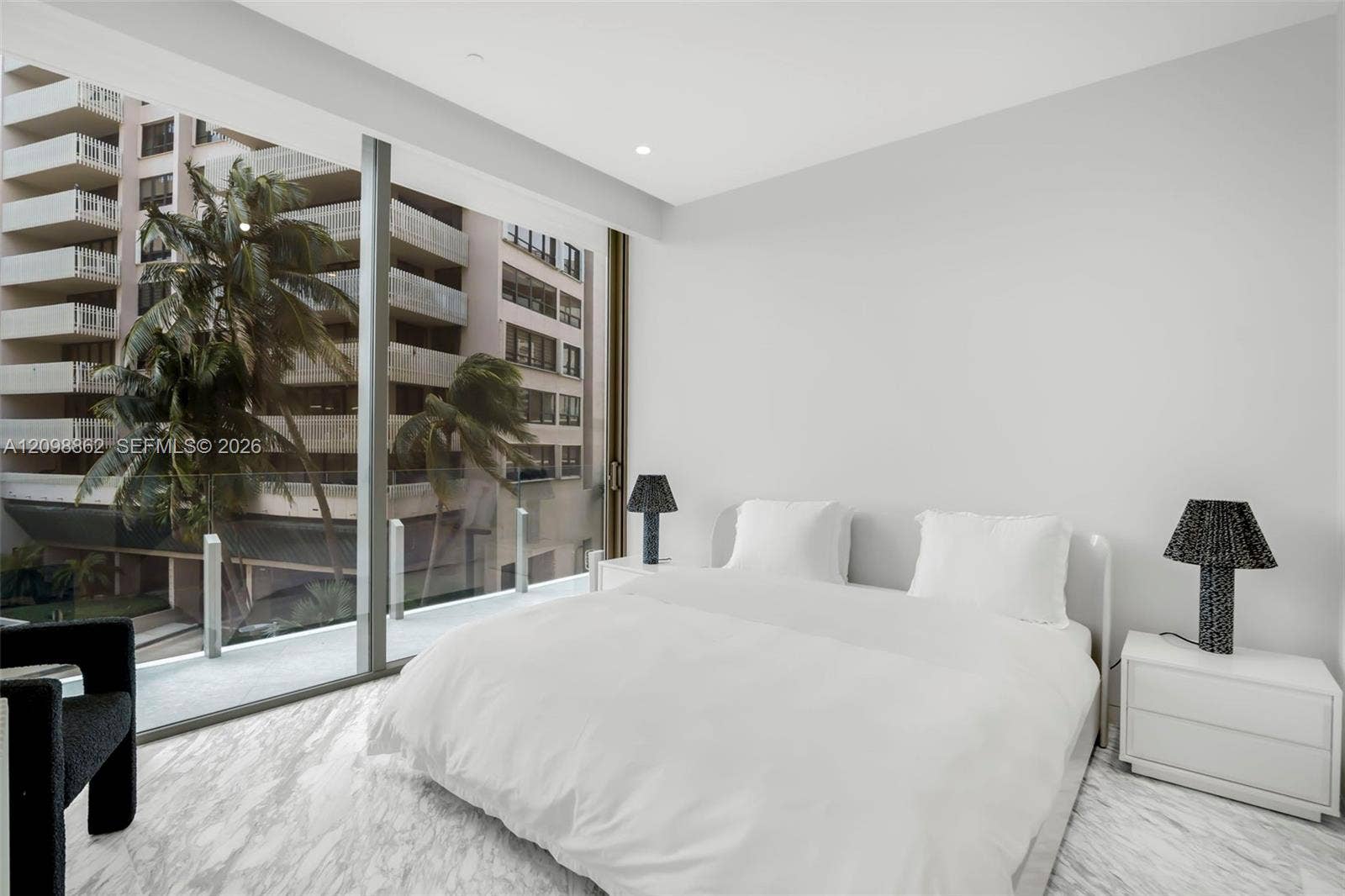 Floor-to-ceiling windows featuring panoramic urban exposures, glass-panel balcony railing, and natural stone flooring