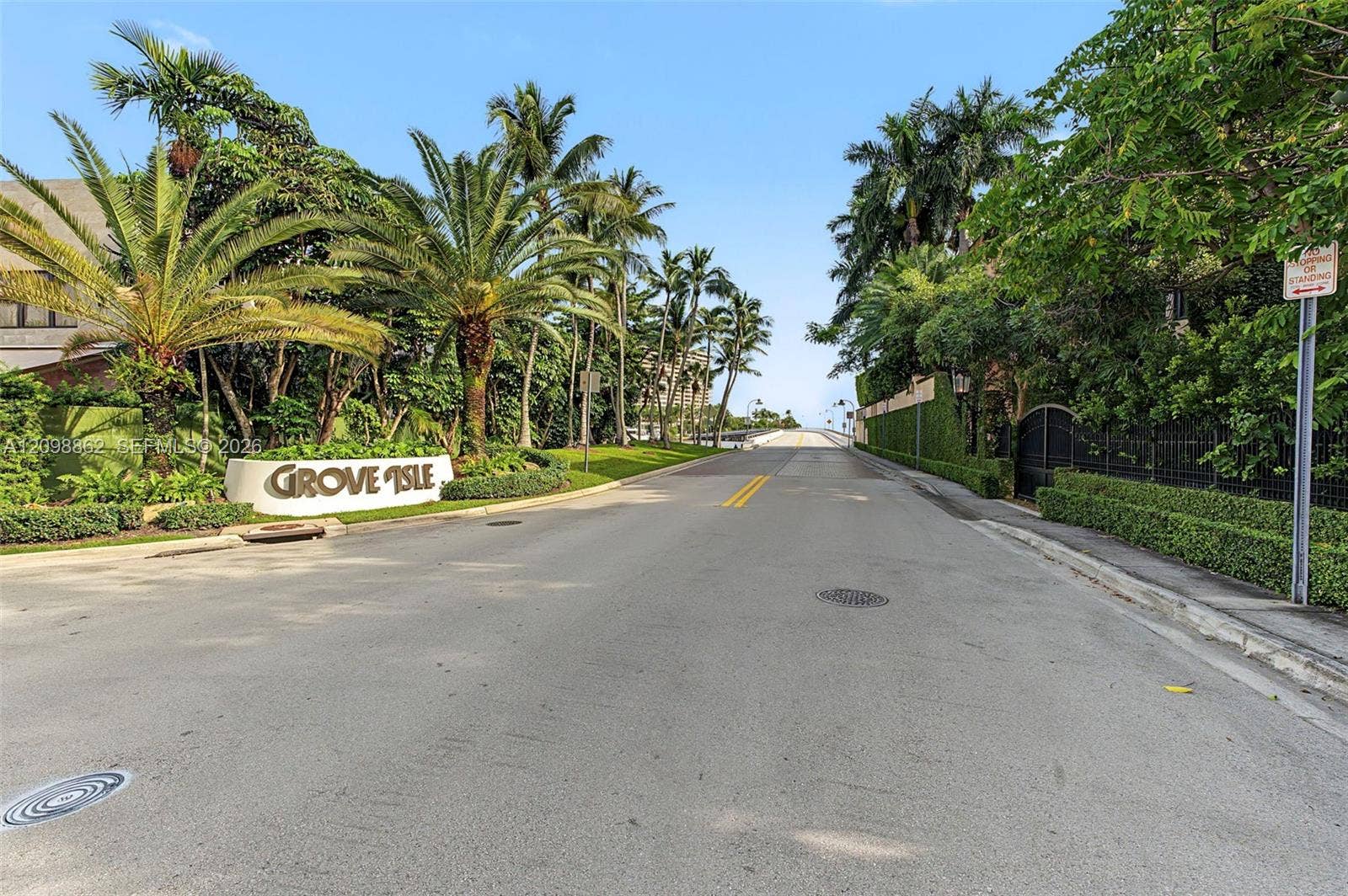 Community entrance featuring mature palm trees, manicured hedges, and professional landscaping