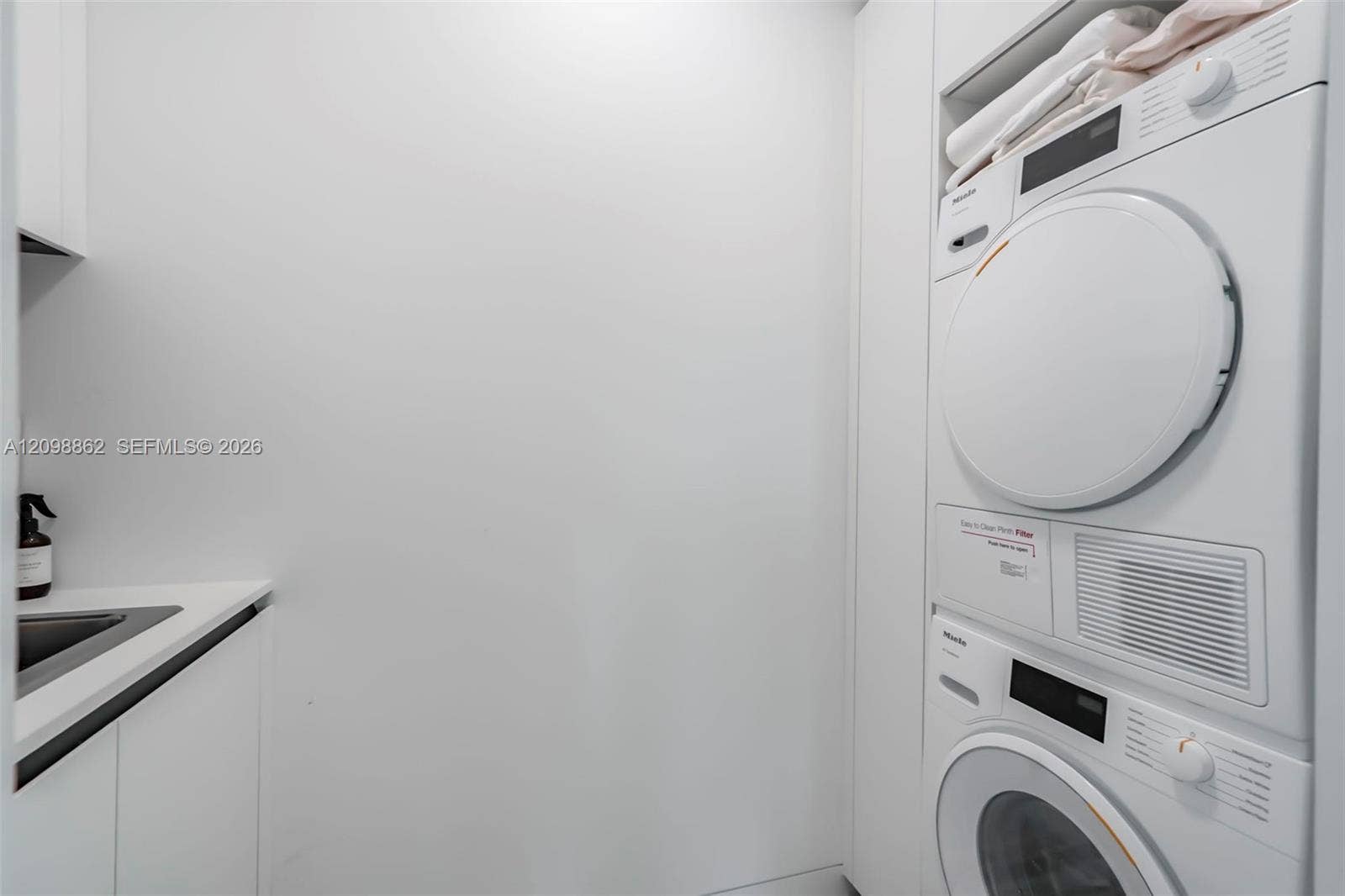 Laundry area featuring stacked white appliances, built-in cabinetry, and a countertop with an integrated sink
