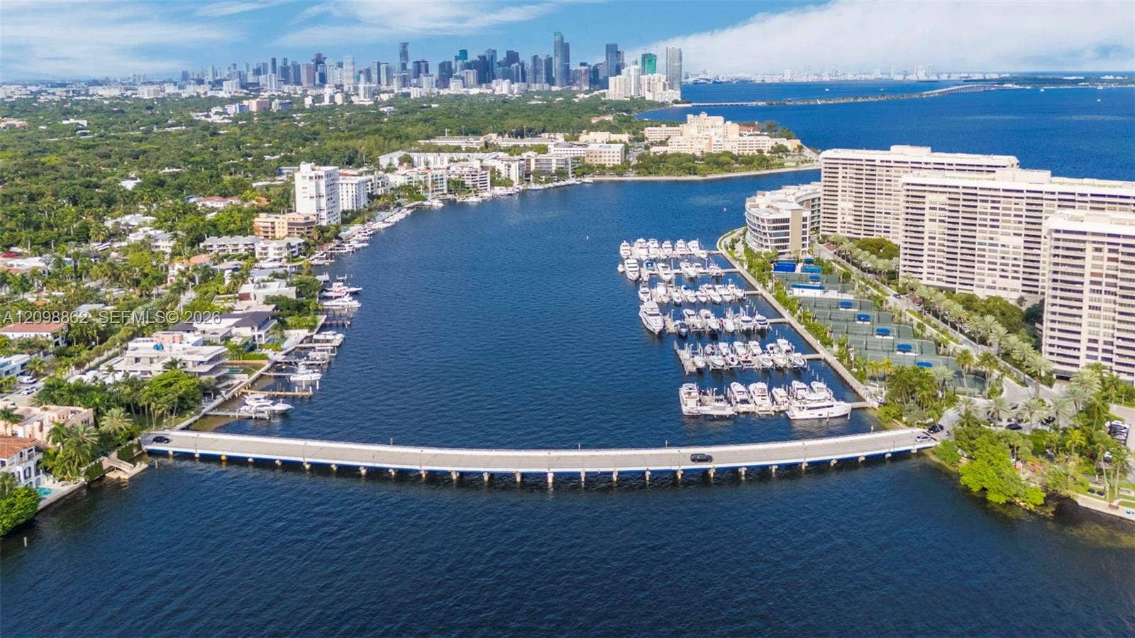Aerial perspective featuring a waterfront marina, deep-water access, concrete bridge infrastructure, and high-rise residential architecture with city skyline backdrop