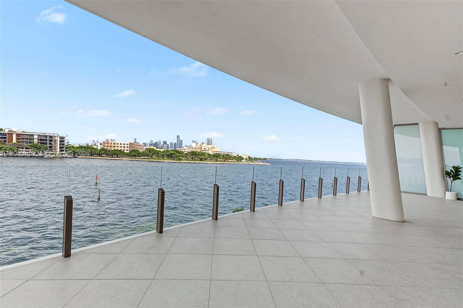 Covered terrace featuring large-format stone tile flooring, structural columns, and a frameless glass railing system