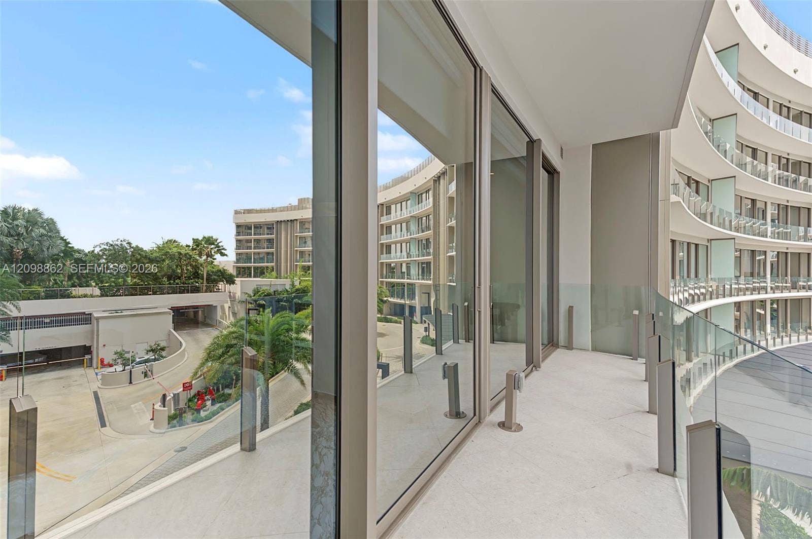 Curved exterior balcony featuring full-height glass sliding doors, stone-tiled flooring, and a glass panel railing