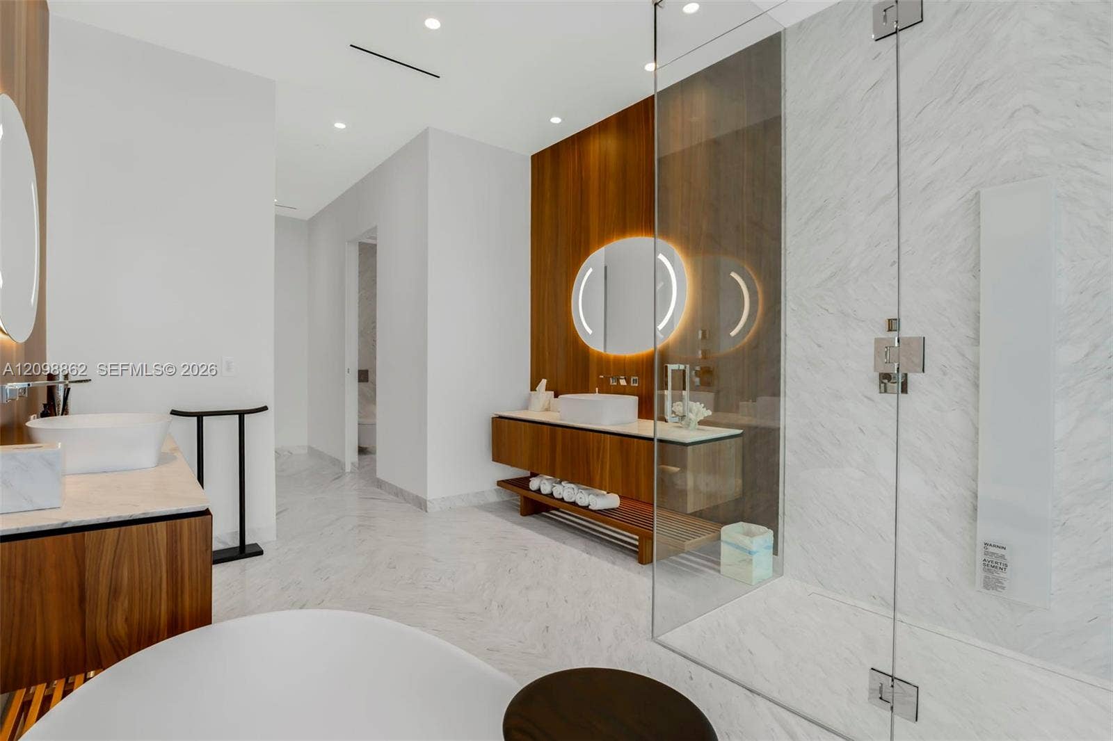 Floating wood-finish vanity with vessel sink, stone-finish flooring, full-height wall paneling, and frameless glass-enclosed shower