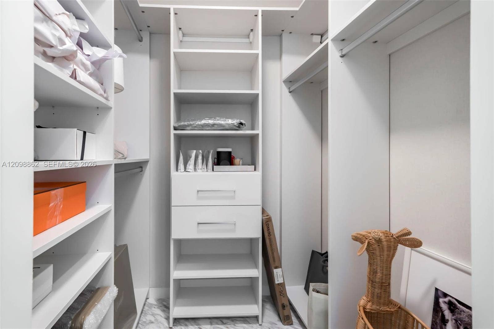 Custom walk-in closet featuring floor-to-ceiling white shelving, integrated hanging rods, built-in drawer storage with polished hardware, and stone-finish flooring