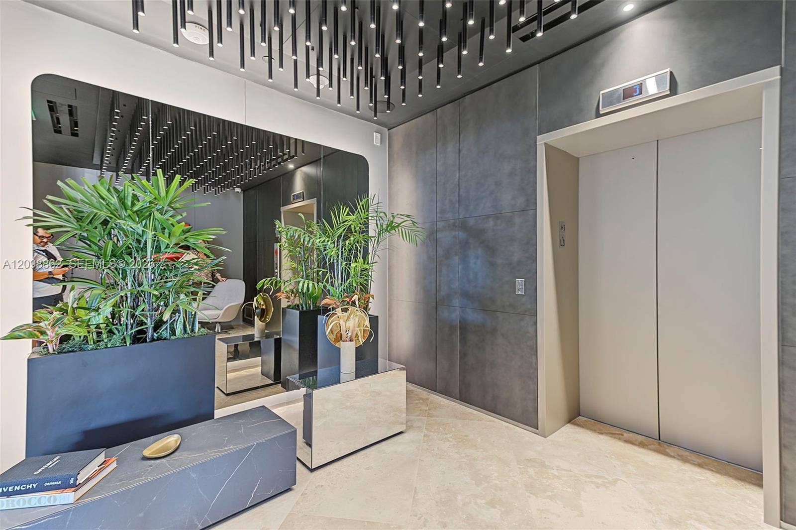 Lobby area featuring large-format stone-look wall paneling, custom-designed vertical pendant lighting, polished stone flooring, and a integrated elevator with metallic doors