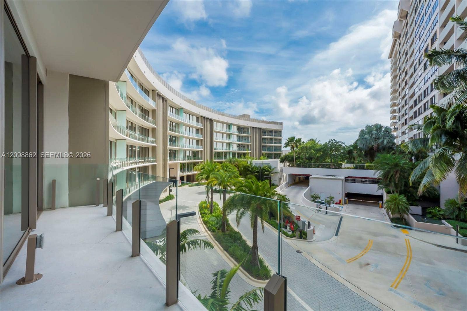 Curved private balcony featuring glass panel railings, concrete flooring, and metal architectural accents