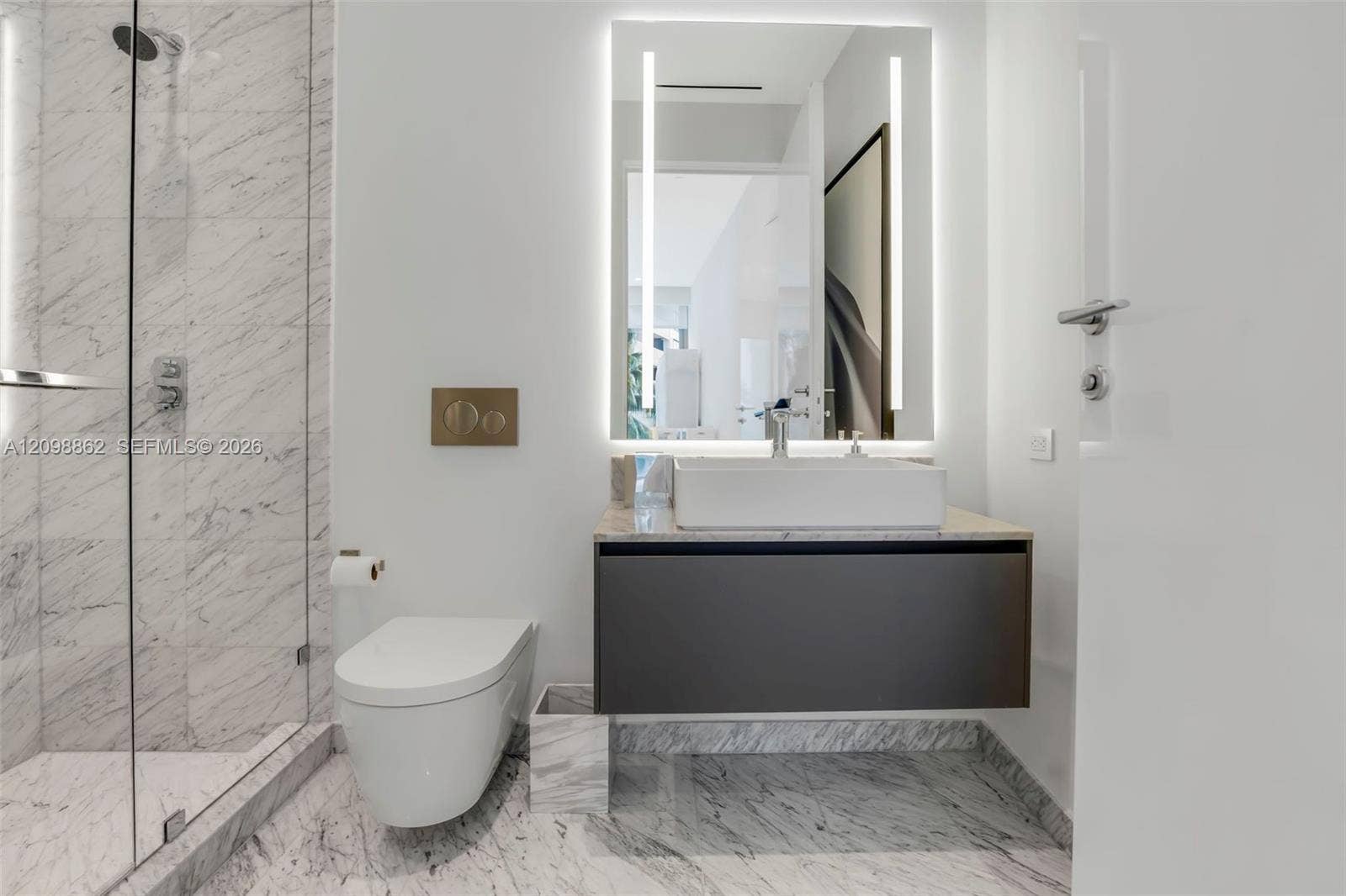 Bathroom featuring a glass-enclosed shower with stone tile surround, floating vanity with a rectangular vessel sink, wall-mounted toilet, illuminated mirror, and stone flooring