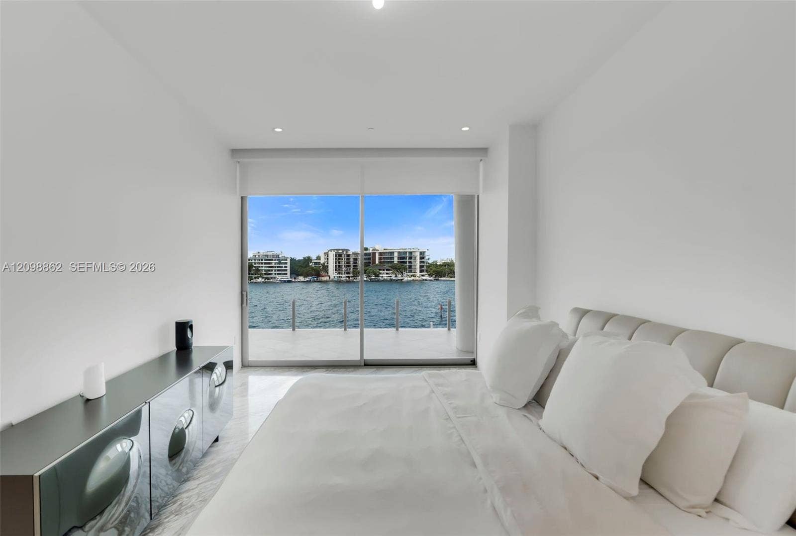 Floor-to-ceiling glass sliding doors, private balcony, water frontage, recessed ceiling lighting, and polished stone-finish flooring