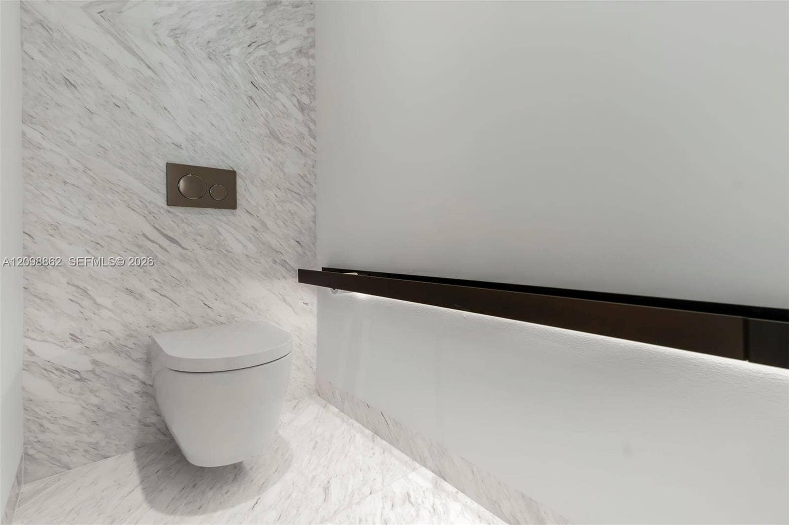 Wall-mounted toilet with stone-finish wall cladding and floor tile, featuring a dual-flush button and a horizontal dark metal accent rail