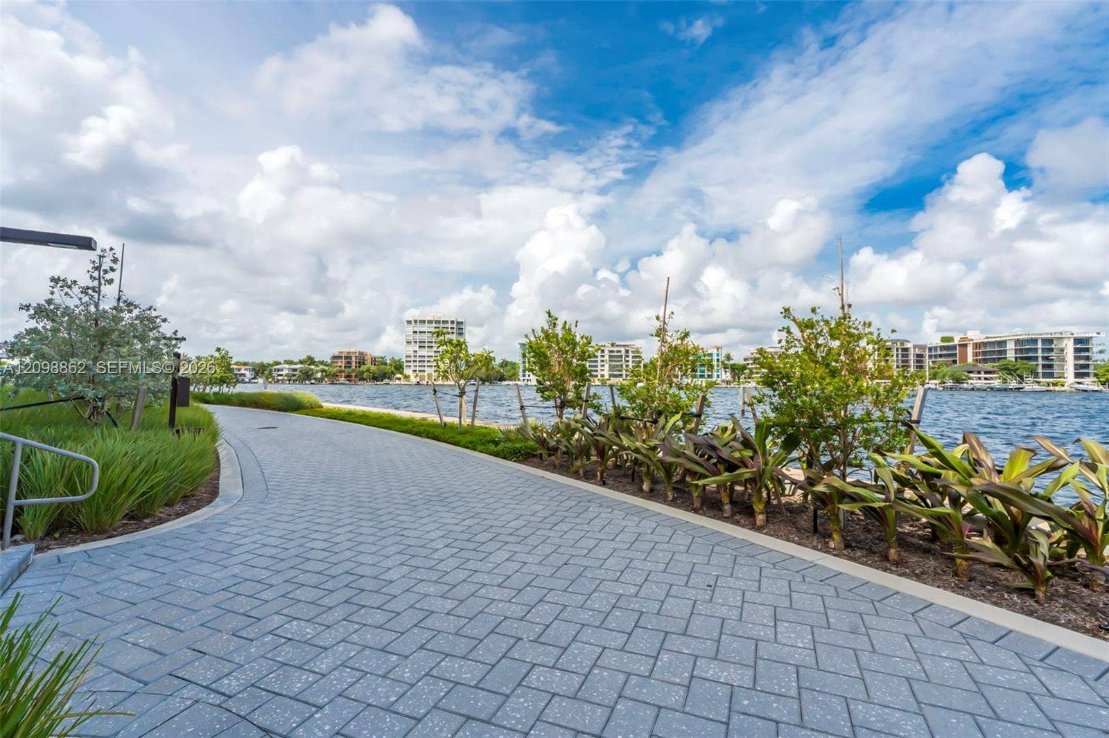 Waterfront walkway featuring concrete paver surfacing, curated tropical landscaping, and metal railing accents
