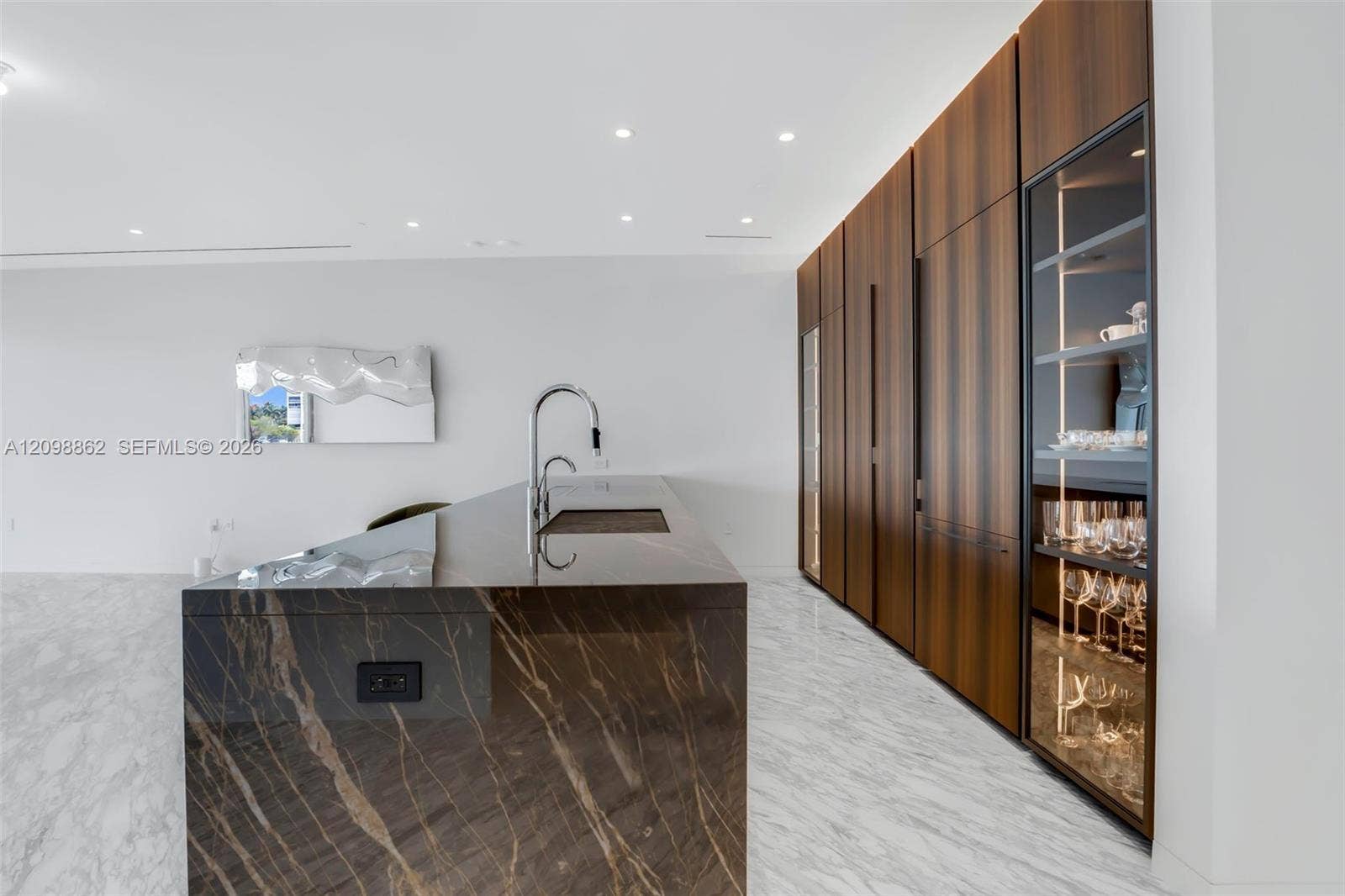 Kitchen featuring a stone-topped island with an integrated sink, full-height wood-finish cabinetry, recessed lighting, and a glass-front display cabinet