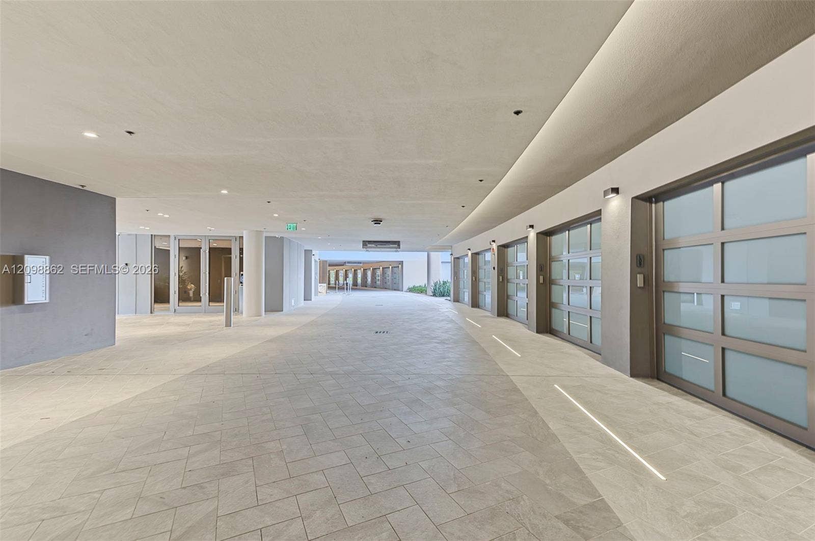 Covered motor court featuring herringbone-patterned stone flooring, tiered LED cove lighting, and multiple garage bays with frosted glass panels