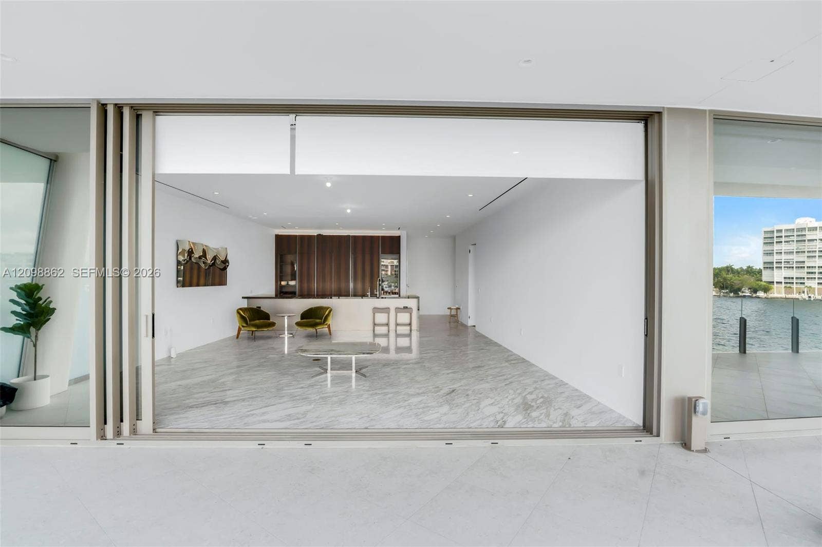 Retractable floor-to-ceiling glass wall, stone-finish flooring, built-in cabinetry, recessed ceiling lighting, and waterfront terrace access