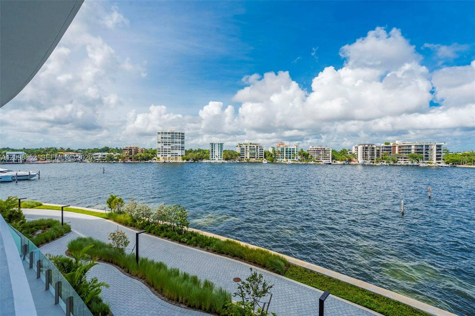Waterfront terrace with a glass railing, paver walkway, landscaped greenery, and direct water frontage