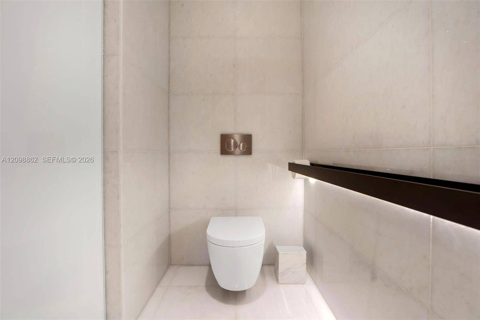 Wall-mounted toilet with a dual-flush actuator plate, floor-to-ceiling large-format tile surround, and integrated linear accent lighting