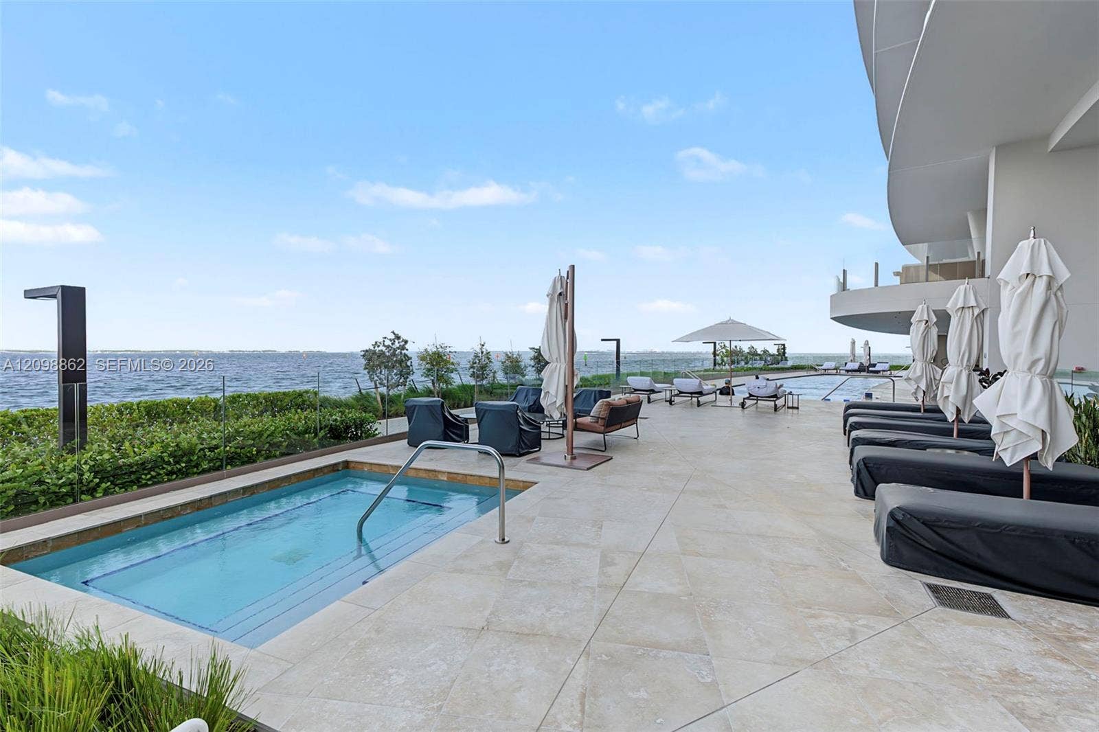 Expansive terrace featuring stone tile flooring, an in-ground spa, glass panel railing, and water frontage
