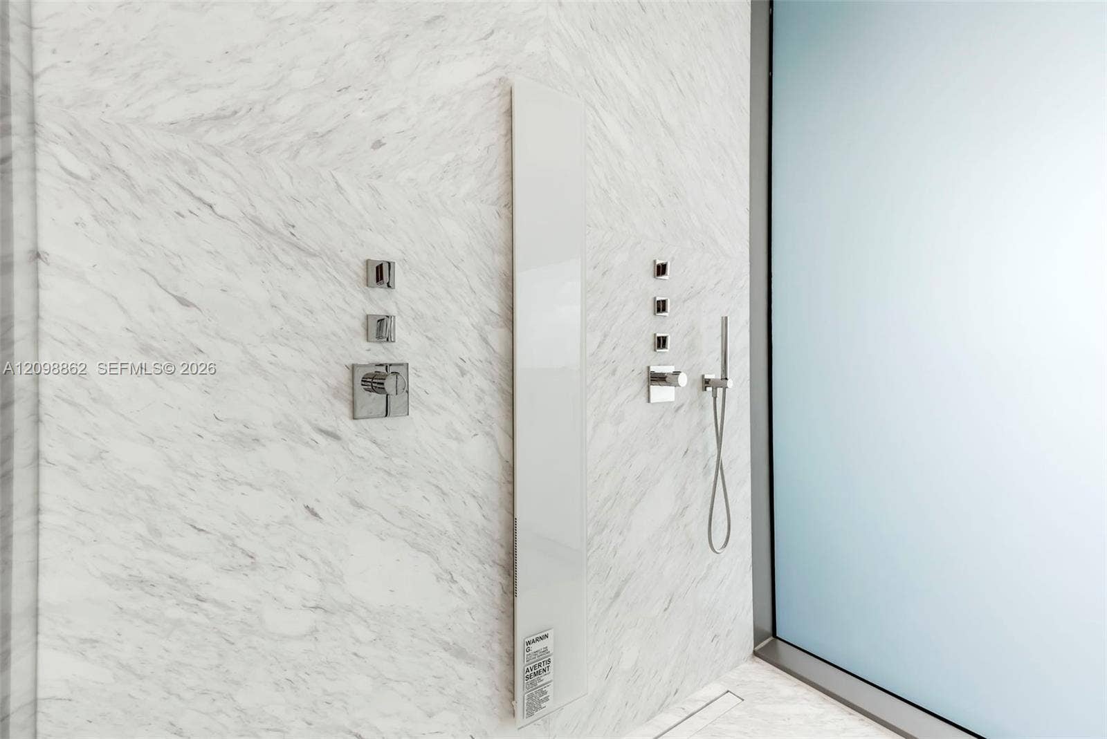 Full-height stone wall tiling, polished chrome dual-function shower controls, integrated vertical shower panel, adjustable handheld shower fixture, and frosted glass paneling