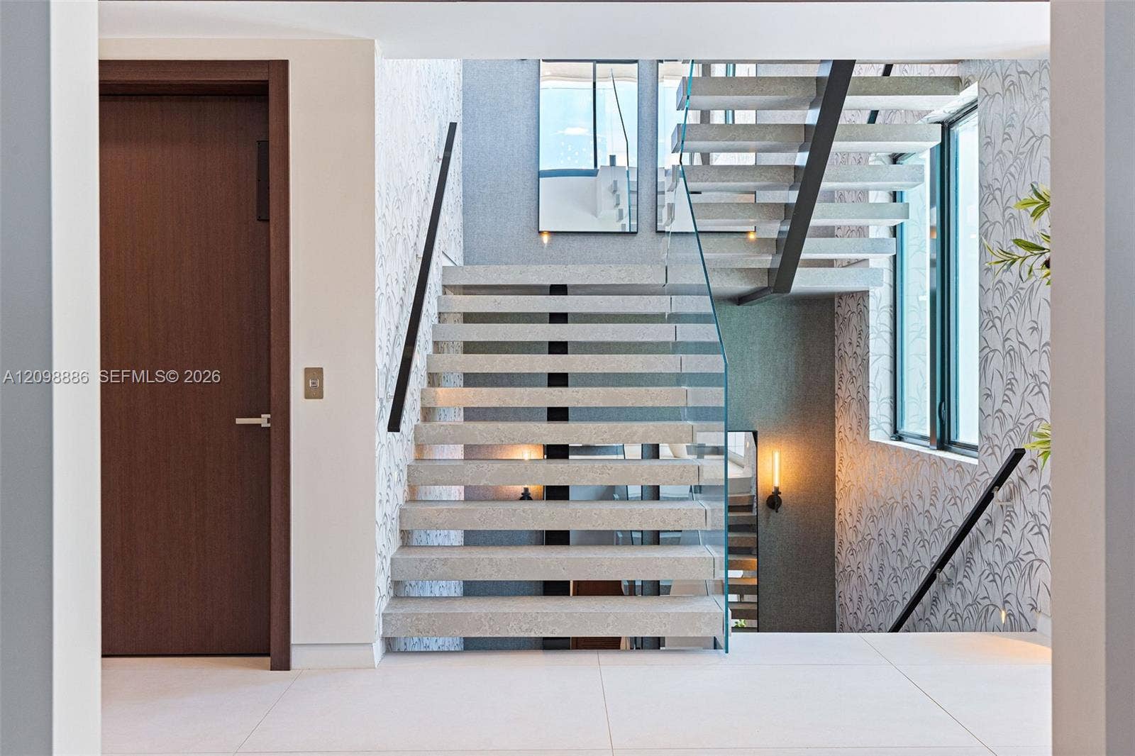 Open-riser staircase featuring terrazzo treads, a glass panel railing, and wall-mounted linear lighting