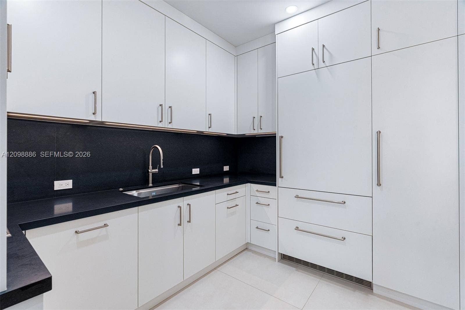 Kitchen featuring flat-panel white cabinetry, contrasting dark stone countertops, integrated panel-ready refrigerator, stainless steel undermount sink with gooseneck faucet, and recessed ceiling lighting